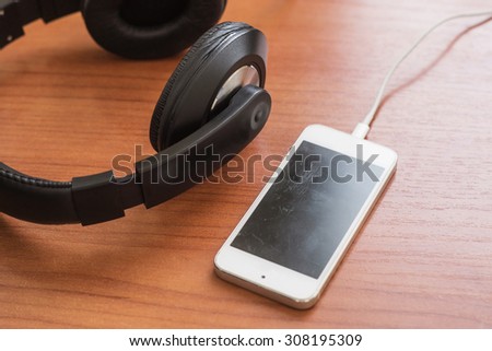 Phone on charge and big headphones lie on a brown wooden table