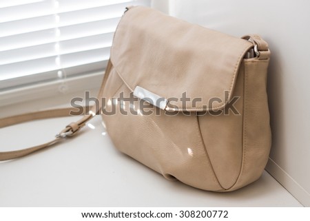 Little beige leather bag on a windowsill with white closed louvers on a sunny day