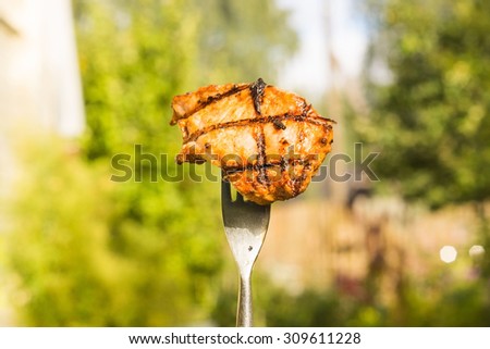 Hand holding a steel folk with cooked piece of meat on a yard near the house in a countryside