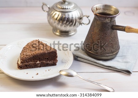 A piece of chocolate cake on a white plate. Turk with hot coffee, napkin and silver spoon. Breakfast in coffee house