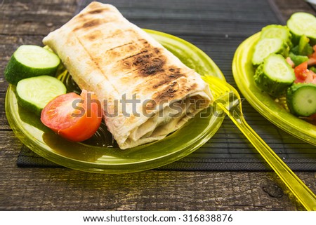 Hot grilled snack for picnic - shaurma with vegetables on a plastic plate with plastic fork