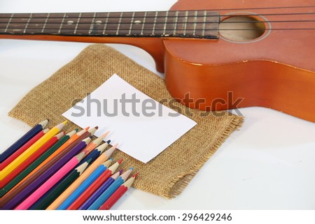 A Ukulele with Colored pencils and paper notes on a white background.