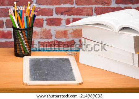 Desk with school supplies and slate in front of brick wall