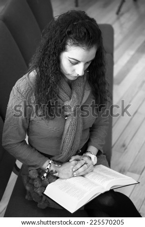 A Hispanic woman folds her hands over the Bible and bows her head in prayer.