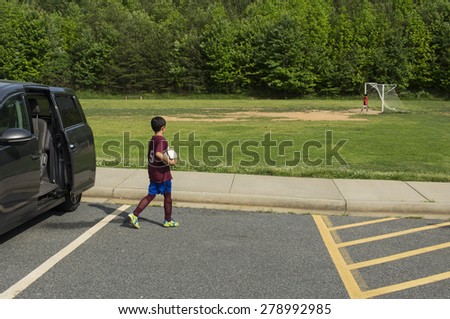A young boy being dropped off for soccer practice. Spring setting, horizontal composition.