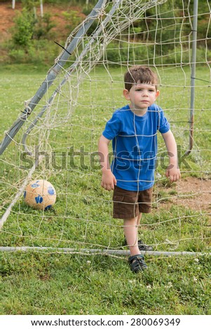 A little boy pressing his face into a goal net, outside on a spring day. He is making a serious face. Vertical.
