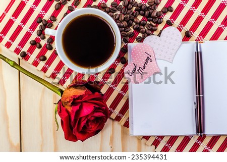 open notepad with cup of coffee and rose on striped napkin