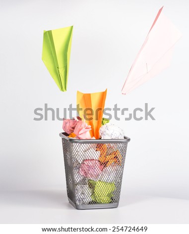 isolated wastebasket full of color waste paper and paper airplane