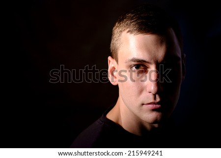 Young serious man on black background in low key