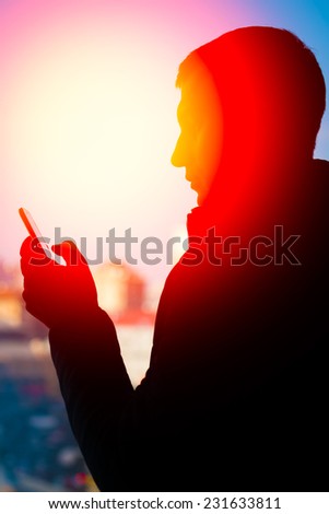 Silhouette of man standing on city background and blue sky. Man holding a telephone. Silhouette, man, sunset, city, phone - advertising concept of freedom of communication.