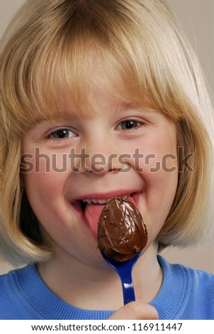 Little girl eating chocolate cream teaspoon.Kid eating nut chocolate cream.