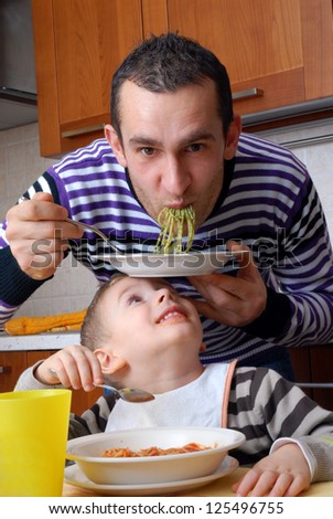Funny father and little kid eating pasta at kitchen.