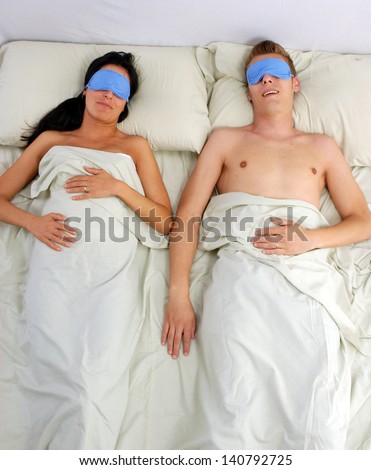Sleeping couple in sleep eye mask on bed.