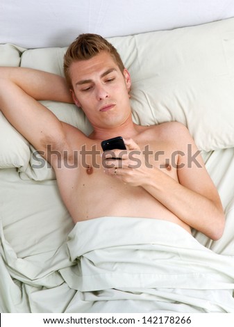 Young man lying down on bed using a cell phone.
