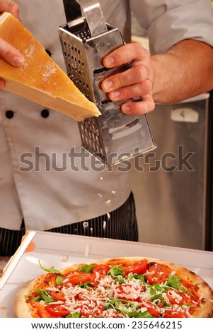 Cook grating parmesan cheese over pizza ready to delivery.