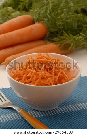 Grated carrots in a white bowl and carrot background.