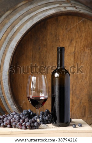 Red wine bottle, cup and grapes on barrels background.