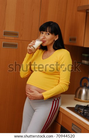Young pregnant woman drinking milk in a kitchen.