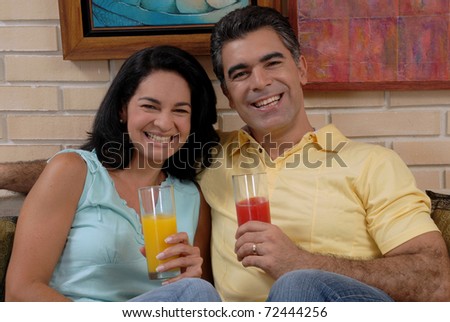 Mid adult couple drinking fruit juice in a living room. Couple drinking and sharing in a living room.