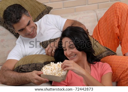 Couple watching tv and eating popcorn. Couple sharing in a living room.