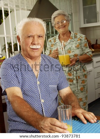 Grand parents drinking and pouring orange juice at kitchen.