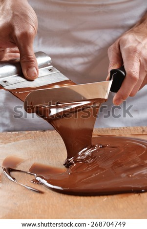Cook mixing chocolate cream with professional chocolate spatula. Melted dark chocolate.