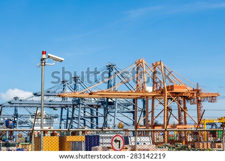 CCTV cameras with warning lights on steel pole and crane in trade port background