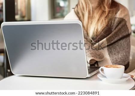Blonde woman in plaid sitting in a cafe with cup of coffee and notebook