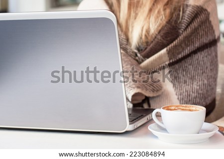 Blonde woman in plaid sitting in a cafe with cup of coffee and notebook