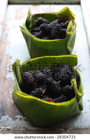two baskets of black mulberry, in a banana leave basket.