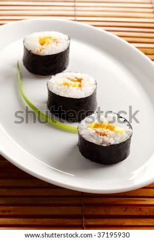 three rolls of sushi, japanese food. On the white plate and places on a bamboo mat.