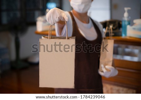 New normal An asian woman wearing gloves and medical face masks delivering take away food bags to customers at the restaurant bar to prevent the spread of corona virus.takeaway concept. space for logo