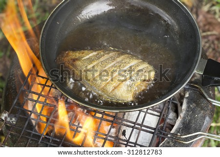 cooking fish frying in oil on the fire on camping  in the forest.