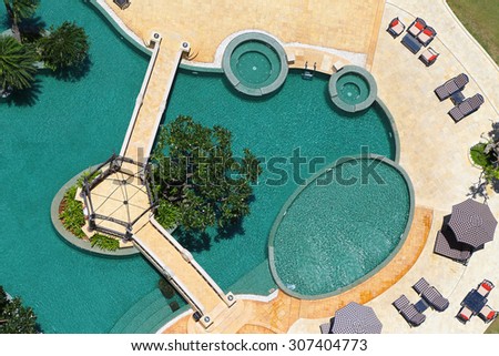 Aquamarine Color Swimming Pool Surrounded by Yellow Marble Shot from Above. A few Palm Trees and Umbrellas Around the Pool