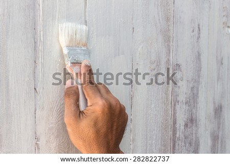 hand worker holding brush painting white on wood fence