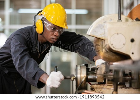 Black male african american workers wear sound proof headphones and yellow helmet working an iron cutting machine in factory Industrial.