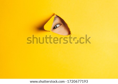 The boy peeks through a cut hole in the yellow paper wall. Human eye closeup. Stock fotó © 