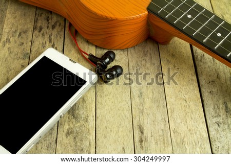 smart phone, earphone and guitar on wood plank