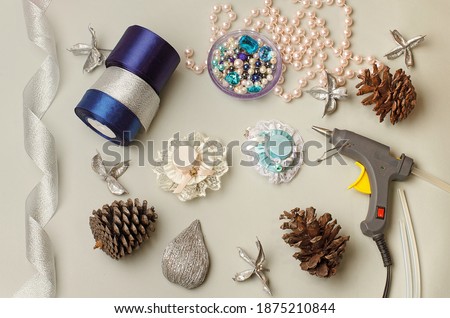 Needlework lessons.Tapes,cloth, glue gun.Hat hair clip.Crafts.DIY.
Shiny ribbon,cones,handcraft tool, ribbon beads on a gray background.Winter crafts. Quarantine session.Handmade.