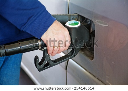 male hand holding gasoline pump into the tank of a car