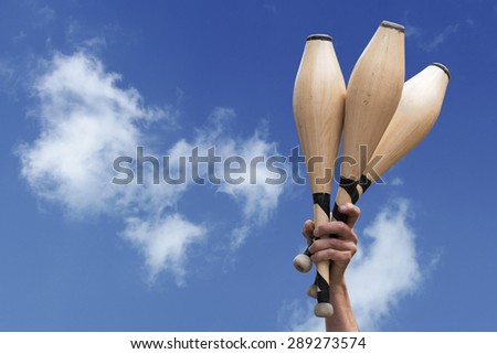 man\'s hand holding three wooden juggling clubs in the blue sky, metaphor for talent, assiduity, skill and success, copy space
