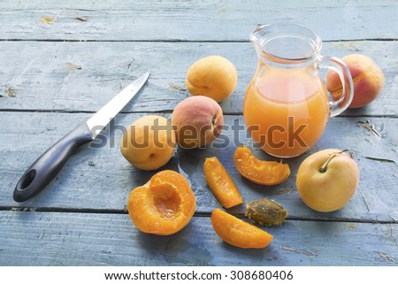 group of apricots, whole and sliced, juice in a glass jug and a knife on an old blue painted wooden table