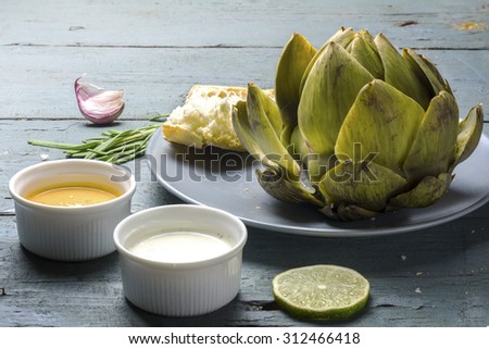 cooked artichoke with dips and bread on a rustic gray blue wooden table
