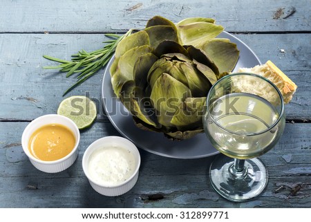 Artichoke cooked with dips, bread and wine on a rustic blue wooden table