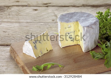 soft blue cheese from France with wedge portion and some herbs on a rustic wooden table