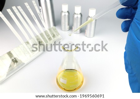 chemical beaker is on the white table with blotting paper , fragrance bottle and essential oil bottle are used to blend the nice scent for making perfume and candle by the perfumer in the laboratory