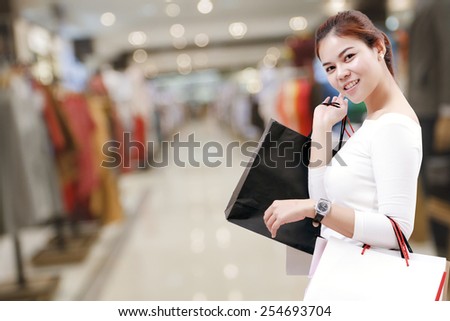 happiness, consumerism, sale and people concept - smiling young woman asian with shopping bags over mall/suppermarket background