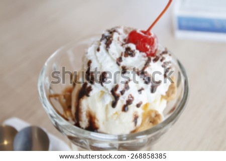blurry Vanilla sundae ice cream with sauce, wafer, sweet cherry, mint and chocolate curls in cup on table