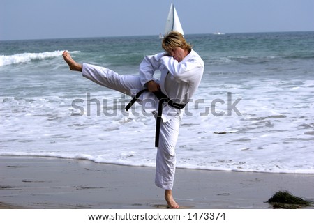 Man with a black belt working out on the beach. Executing a  kick