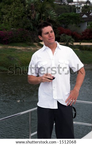 A young man drinking a glass of wine on a private yacht and giving a cocky look